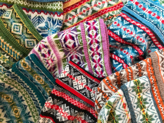 Ten colorful Fair Isle fisherman keps (or caps or hats) piled atop a table